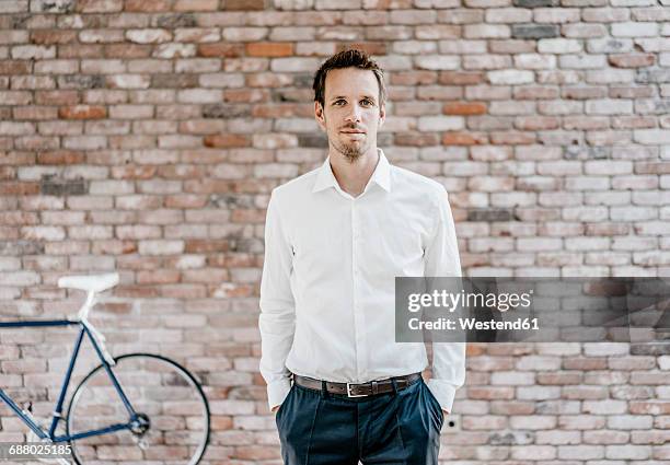 portrait of confident businessman in front of brick wall - dichtknopen stockfoto's en -beelden