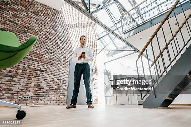 smiling businessman in office with cell phone - person standing front on inside stock pictures, royalty-free photos & images