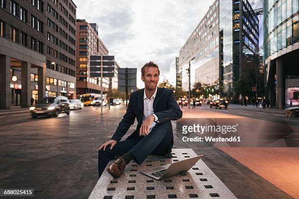 germany, berlin, potsdamer platz, businessman sitting on bench with laptop in the evening - berlin business fotografías e imágenes de stock