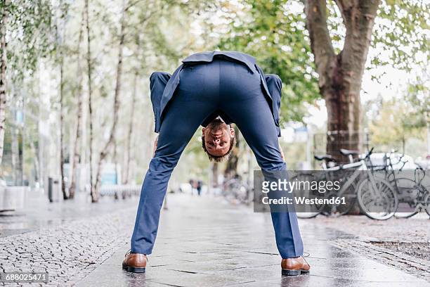 back view of businessman bending over on pavement looking through his legs - bogen stockfoto's en -beelden