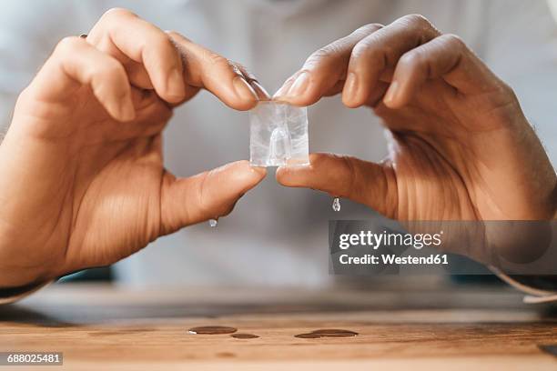 hands of man holding melting ice cube - aggregation stage stock pictures, royalty-free photos & images