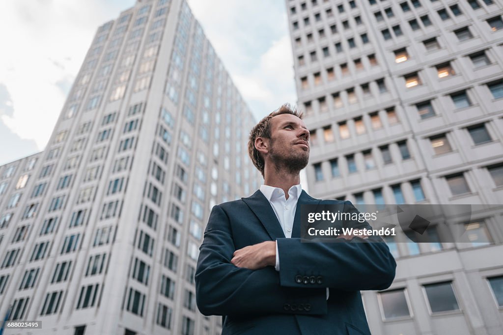 Germany, Berlin, Potsdamer Platz, businessman with arms crossed standing in front of luxury hotel