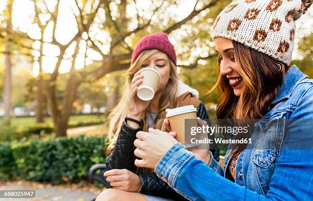 two young women drinking coffee in a park in autumn - autumn friends coats stock pictures, royalty-free photos & images