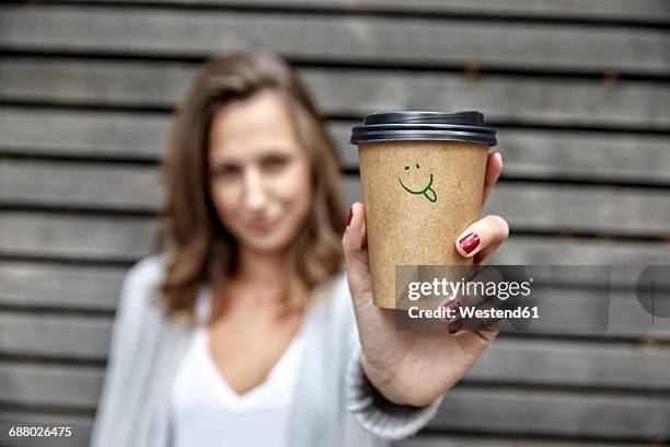 young woman holding takeaway coffee cup with smiley face - coffe to go becher stock-fotos und bilder