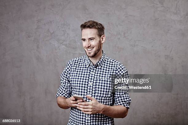 smiling young man holding cell phone - regard de côté studio photos et images de collection