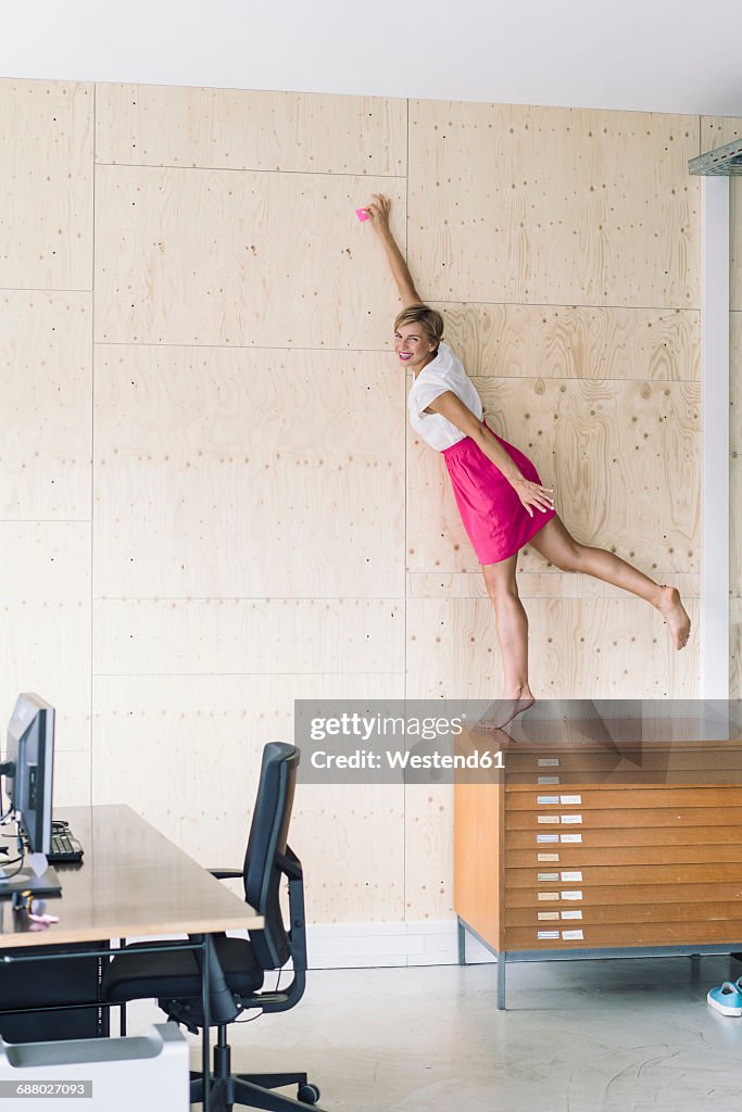 Businesswoman putting sticky note on wooden wall