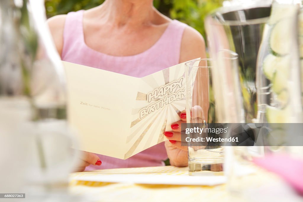 Senior woman sitting in garden, holding birthday card