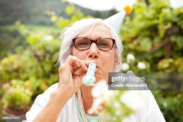 senior woman blowing party blower - party blower stock-fotos und bilder