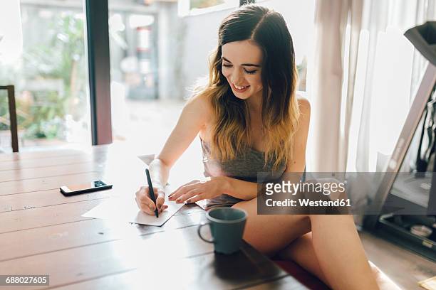 smiling young woman writing at home - correspondence stock pictures, royalty-free photos & images