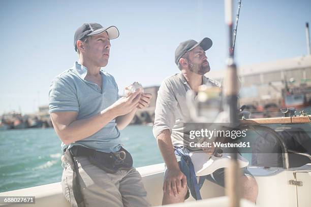 two men having lunch break on boat with fishing rods - deep sea fishing stock-fotos und bilder