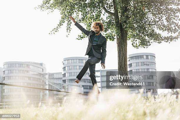 young businessman balancing on slackline - slacklining stock-fotos und bilder