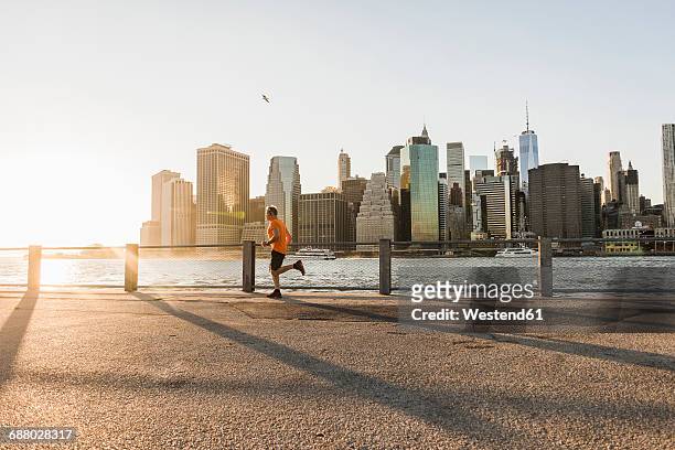 usa, brooklyn, man jogging in front of manhattan skyline in the evening - brooklyn new york foto e immagini stock