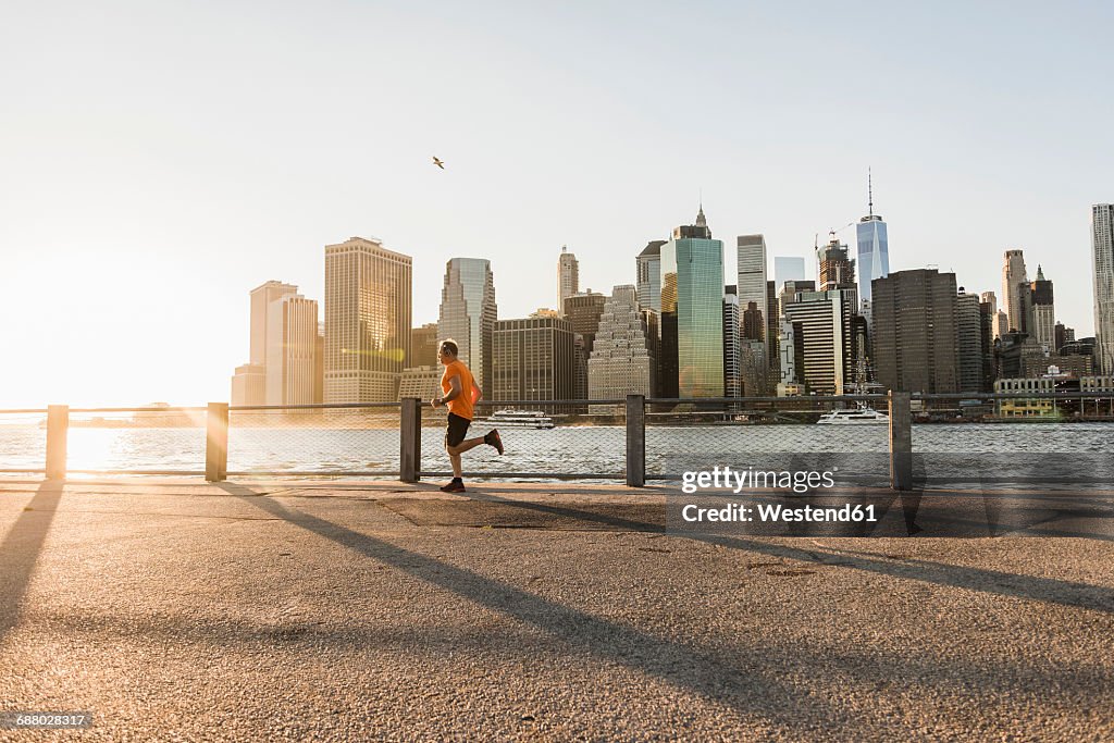 USA, Brooklyn, man jogging in front of Manhattan skyline in the evening