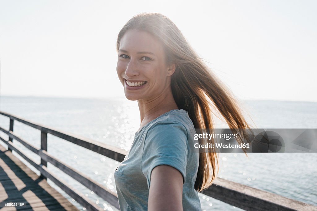 Portrait of happy young woman on jetty at backlight