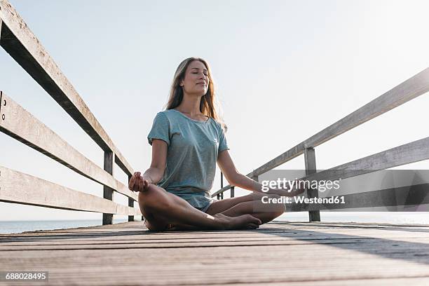 young woman practising yoga on jetty - schneidersitz stock-fotos und bilder