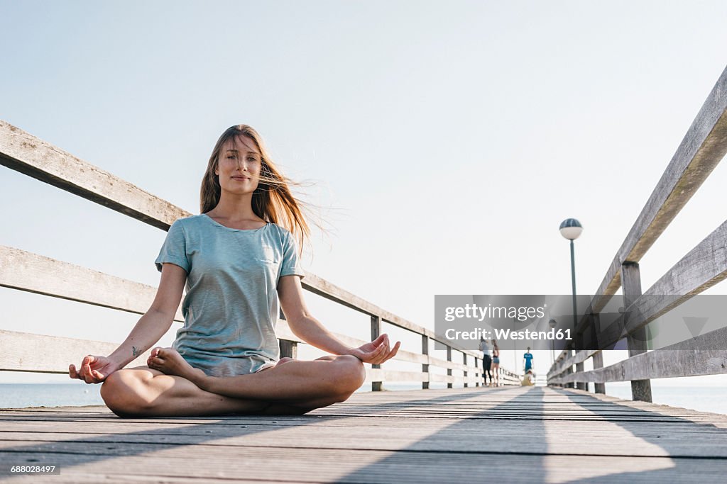 Young woman practising yoga on jetty
