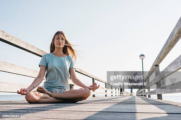 young woman practising yoga on jetty - lotus position stock pictures, royalty-free photos & images