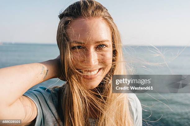 portrait of happy young woman with blowing hair in front of the sea - woman wind in hair stock pictures, royalty-free photos & images