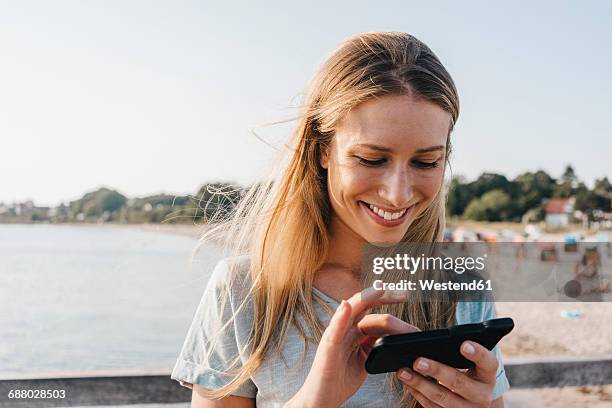 smiling young woman using smartphone - woman smartphone nature stockfoto's en -beelden
