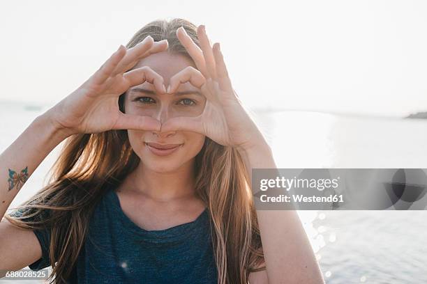 portrait of young woman forming heart with her hands - blonde glasses stock-fotos und bilder