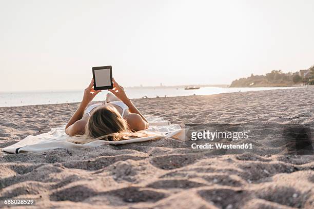 young woman lying on blanket on the beach using tablet - e reader stock-fotos und bilder