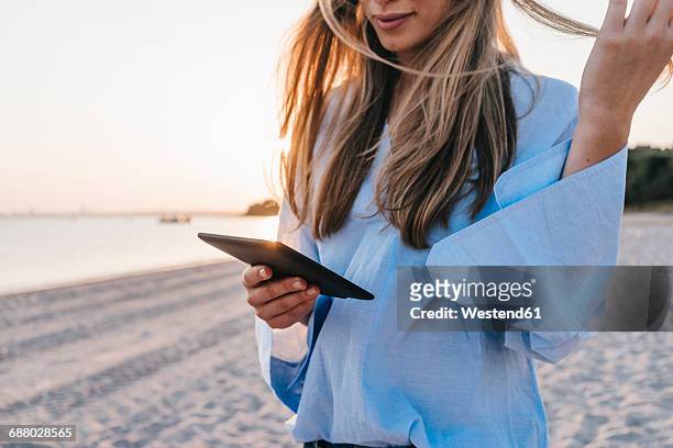 young woman using tablet on the beach, partial view - frau haarsträhne blond beauty stock-fotos und bilder