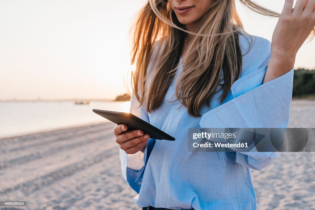 Young woman using tablet on the beach, partial view