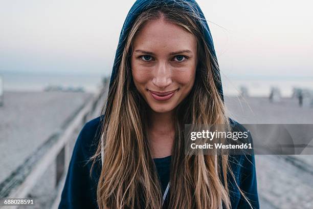 portrait of smiling young woman wearing hooden jacket standing on jetty - pedestrian walkway stock-fotos und bilder