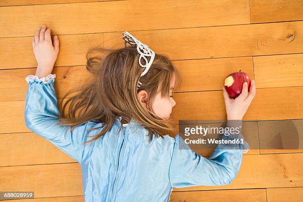 little girl lying on wooden floor holding bitten red apple - child mortality stock pictures, royalty-free photos & images