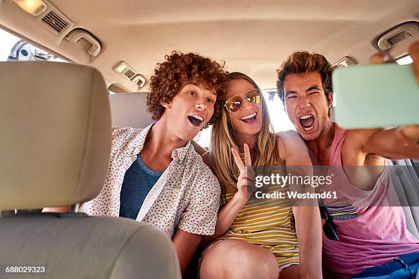 happy friends in a car taking a selfie - three people in car stock pictures, royalty-free photos & images