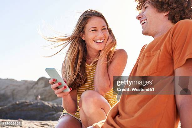 happy couple with cell phone on the beach - happy couple using cellphone stockfoto's en -beelden