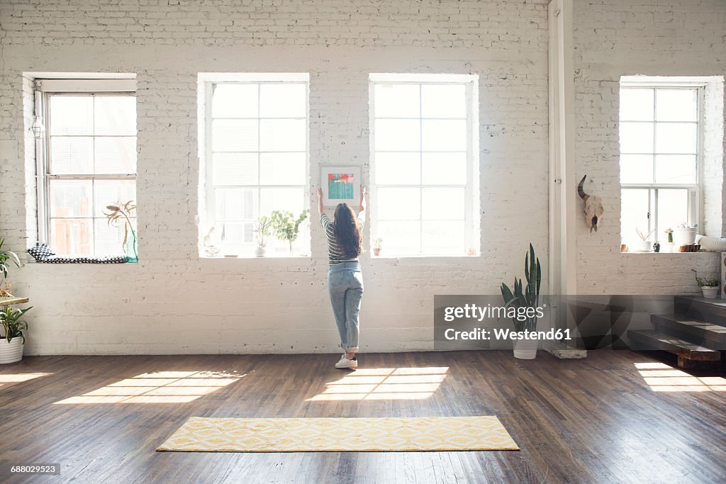 Young woman attaching picture frame to brick wall in a loft