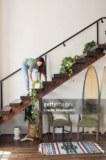 Young woman on stairs in a loft caring for potted plant