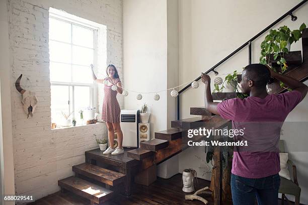 young couple decorating loft with fairylights - positioned stock pictures, royalty-free photos & images