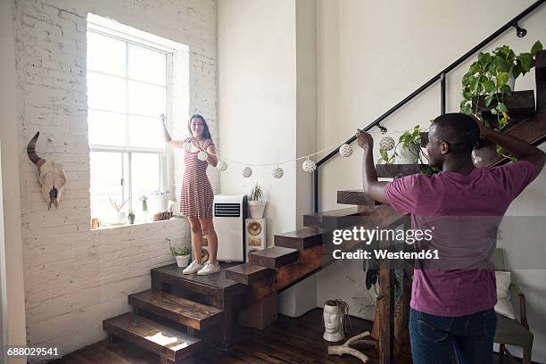 young couple decorating loft with fairylights - decorating loft imagens e fotografias de stock