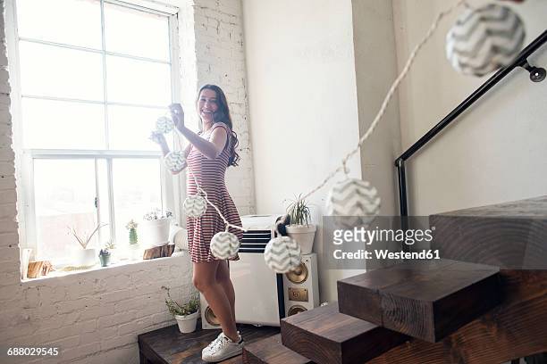 young woman decorating loft with fairylights - decoration stock-fotos und bilder