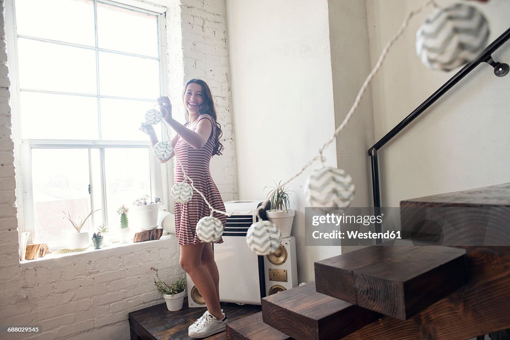 Young woman decorating loft with fairylights
