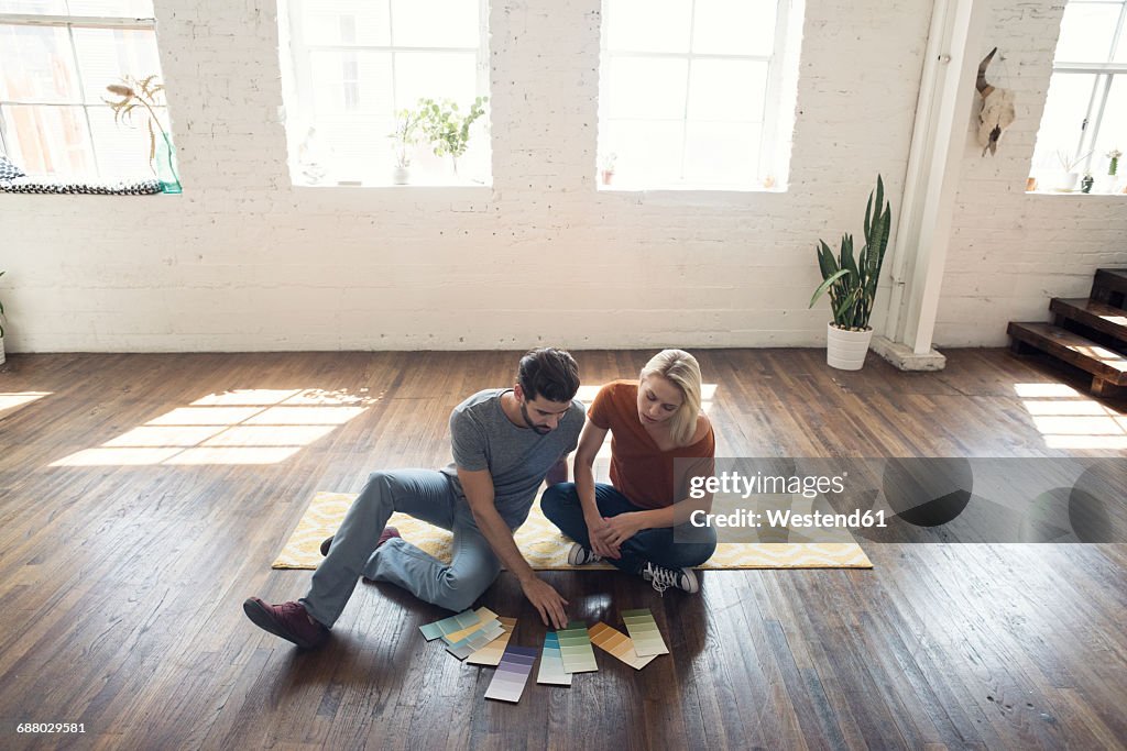 Young couple sitting on carpet in a loft looking at color samples