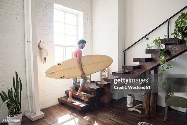 young man carrying a surfboard on stairs in a loft - apartamento tipo loft fotografías e imágenes de stock