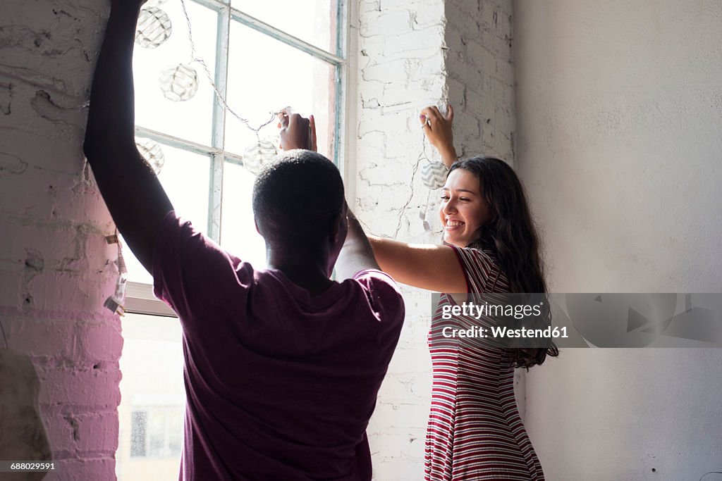 Young couple decorating window with fairylights