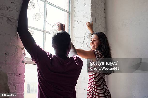 young couple decorating window with fairylights - decorating loft imagens e fotografias de stock