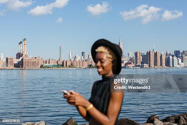 usa, new york city, brooklyn, smiling young woman at east river with manhattan skyline in background - north america skyline stock pictures, royalty-free photos & images