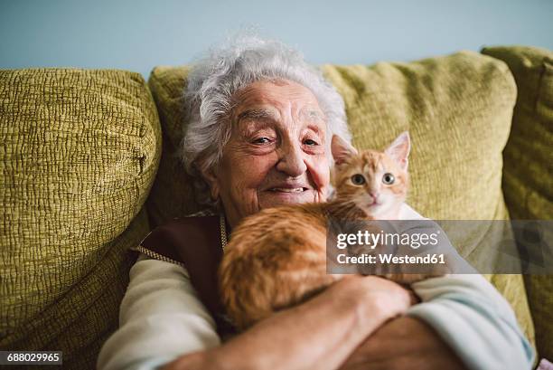 portrait of happy senior woman cuddling with her cat on the couch - cat cuddle stockfoto's en -beelden