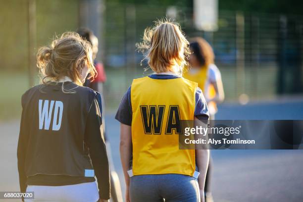 netball players standing side-by-side during match on outdoor court - sporthesje stockfoto's en -beelden