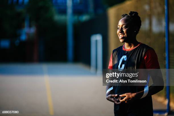 portrait of young woman smiling and wearing netball bib in outdoor, urban sports court - sporthesje stockfoto's en -beelden