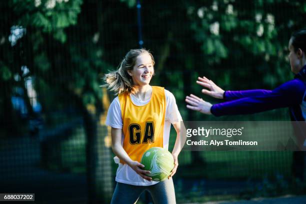 young woman playing netball and being marked on outdoor court in city park - sports bib stock pictures, royalty-free photos & images