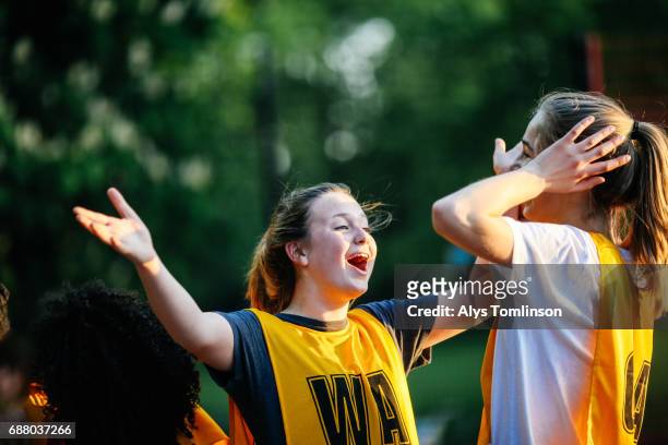netball player laughing with arms out towards teammate during match on outdoor court - practice stock pictures, royalty-free photos & images