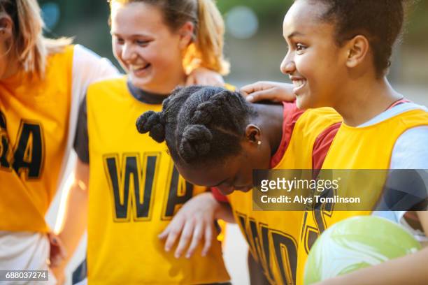 team of young netball players laughing with arms around each other on outdoors netball court - netball team stockfoto's en -beelden