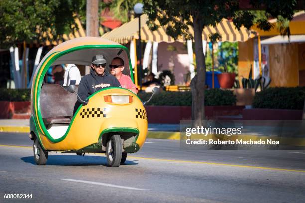 Traditional 'coco-taxi' : Close up of a yellow and green auto-rickshaw carrying a passenger on a calm road.