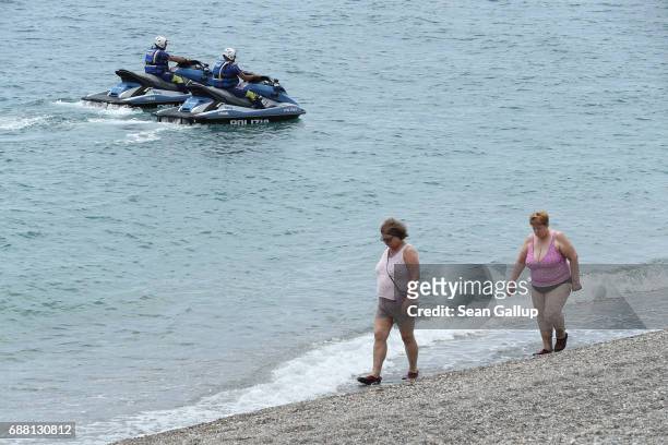 Visitos walk on the beach as police on jet skis ride past near the media center for the G7 Taormina summit on the island of Sicily on May 25, 2017 in...